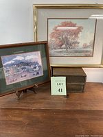 Two framed prints with country scenes displayed on a table, one larger with autumn tree and one smaller with horses and carriages.