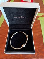 Silver Pandora bracelet with heart-shaped charm inside a white box with a black velvet interior and Pandora branding.