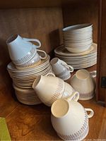 Stacked cups and saucers with gold decor inside wooden cabinet.