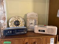 Overview of four-piece lot: United wall clock, white crackle finish mantel clock, Citizen cassette recorder radio and Concerto flip clock radio