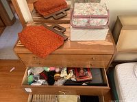 Wooden drawer open showing yarn, knitting needles, crochet hooks and other sewing supplies inside, with orange fabric knitting bag and floral fabric sewing box on top of the drawer
