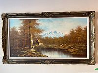 Full view of framed oil painting showing landscape with pond, trees, cabin, and mountains.