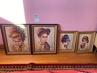 Four framed Medeiros prints of children lined up against pink wall and on wooden floor, showing detailed children's portraits with various hairstyles and accessories.