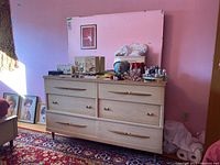 Front angle of wood laminate dresser with items on top and pink room background showing condition and styling.