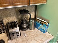 Overview photo of 4 small kitchen appliances on countertop showing toaster, blender, electric kettle, and boxed hand mixer.