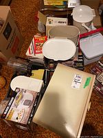 Overview of collection of small appliances and kitchen items including boxes, cooler, slicer, bread box, and containers.