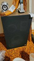 Two large Aura Audio wood laminate box speakers covered in black fabric with metal Aura Audio Inc logo plaques on the lower front corner.