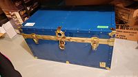 Front side view of the large blue metal trunk with brass latches and lock; trunk is rectangular and appears in good vintage condition.