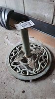 Full view of umbrella stand base and pole showing circular openwork decorative design with leaves and scrolls.