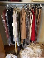 Wide view showing hanging women’s clothing items on rack with plastic garment covers on some pieces.