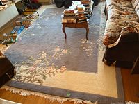 Rug displayed in living room setting showing the full size and floral patterns in blue and cream colors.
