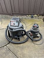 Photo showing both shop vacuums outside on concrete, hoses and power cords attached.
