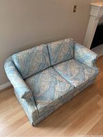 Front angle view of love seat couch showing the two seat cushions and rolled armrests in pastel abstract fabric upholstery.