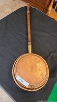 Full view of the antique bed warmer showing round copper pan with flat bottom, hinged lid, and long turned wooden handle with brass collar.