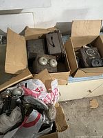 Overall view of three boxes filled with various antique telephone parts including wood ringer units, metal crank boxes, and scattered parts.