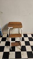 Front view of the antique step stool showing wooden top and two steps with white metal frame.