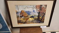 Framed watercolour painting showing autumn rural landscape with path, trees, buildings, and mountains.