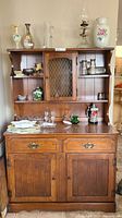 Front view of two-piece wooden china cabinet with various glass and ceramic items on shelves.