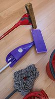 Close-up photo showcasing the red and black Swiffer-type mop with sponge head, purple mop, gray mop head, and red plastic bucket