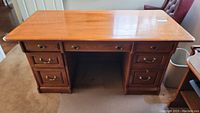 Front view of oak desk showing entire desk with seven drawers, polished oak wood surface with marks visible on top, brass handles on drawers.