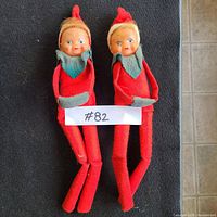 Two vintage elf dolls with red felt bodies, pointed red hats, blue collars and painted plastic faces sitting side by side.