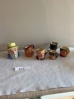 Full view of the six fine china character mugs arranged on a white cloth surface showing all mugs and their distinct facial designs