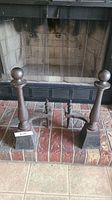 Front view of pair of heavy metal andirons placed in fireplace on brick hearth.