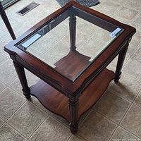Side angled view showing the mahogany frame, glass inset top, decorative legs, and lower shelf