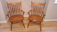Pair of maple dining chairs side by side showing full seats, backs, armrests, and legs on wood floor.