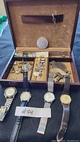 Full view of jewelry box with watches, tie pins, belt buckles, and cuff links inside.