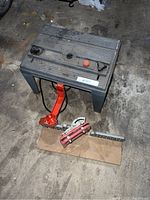 Photo of mitre saw box with orange clamp and red holding mechanism on wooden base, angled view.