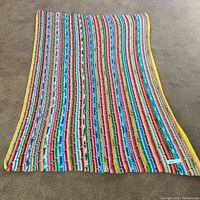 Full view of the blanket laid flat on carpet showing multi-colored ripple stripe pattern with yellow edge border.