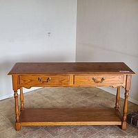 Full front view of the wooden sofa table showing two drawers, turned legs, and lower shelf on tiled floor.