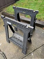 Two Stanley black plastic sawhorses side by side on patio with visible foldable legs and Stanley branding.
