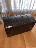 Front angled view of the vintage wooden chest showing domed lid and metal straps with embossed designs.