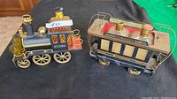 Front angled view of the black and brass metal antique train set showing the locomotive with a glass decanter body for whiskey and attached drinking glasses, alongside the passenger car labeled 'Gin' with two brass bottle caps and a mesh side.