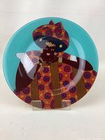 Full view of the round glass plate with the African woman artwork on a turquoise background.
