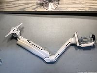Full view of white metal monitor mounting arm showing the flat monitor attachment plate and arm segments with joints.