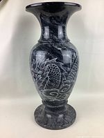 Full view of the vase showing its shape, polished black stone finish with white carved dragon design and round base.