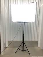 Front view of one illuminated studio softbox light on adjustable tripod stand against corrugated cream background.