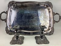Photo showing full view of rectangular silverplated tray with two matching silverplated candlesticks in front, highlighting ornate engravings and tarnish.