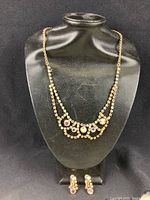 Full view of vintage necklace on black display bust with matching clip-on earrings at base.