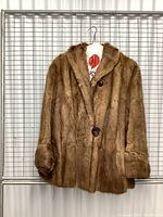 Full front view of a brown rabbit fur coat hanging on a wire grid backdrop