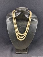 Full view of the triple strand pearl necklace displayed on a black bust stand showing the three graduated strands.