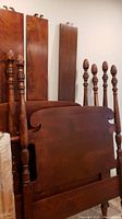 Two dark mahogany twin bed frames disassembled showing headboards, footboards with carved finial posts and side rails.