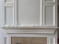 Full set of assorted clear glasses displayed on a white mantelpiece with three sizes and styles.