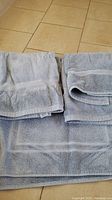 Light blue bath towels neatly folded on tile floor showing texture and decorative border