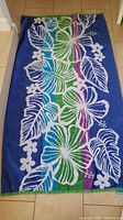 Blue, green, purple striped towel with white tropical design laid on floor.