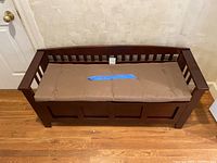 Full front view of wooden bench with padded beige cushion on top.