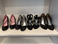 Front view of four pairs of ladies black dress shoes arranged in a row showing different styles and finishes.